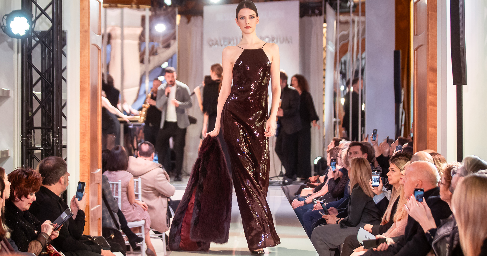 Model walks down the runway in a shimmering burgundy evening gown.