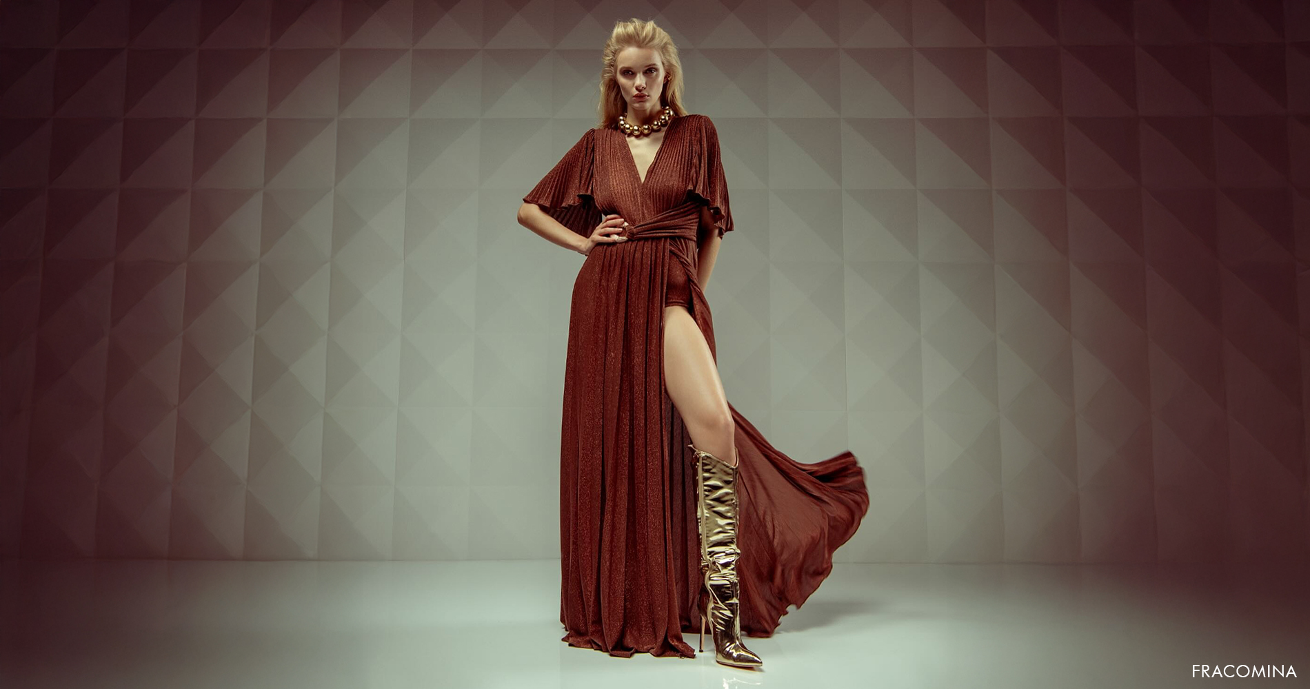 Ženska v razkošni rdeči večerni obleki z visokim razporkom, obuta v zlate čevlje.