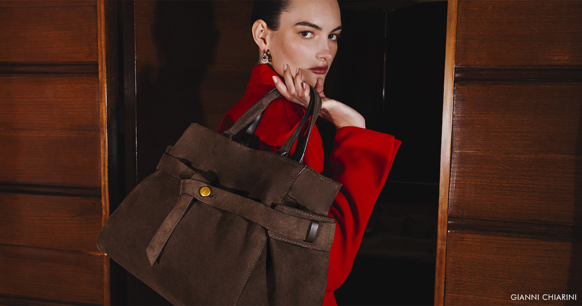 Woman in a red blazer with a large brown suede bag featuring a decorative strap.