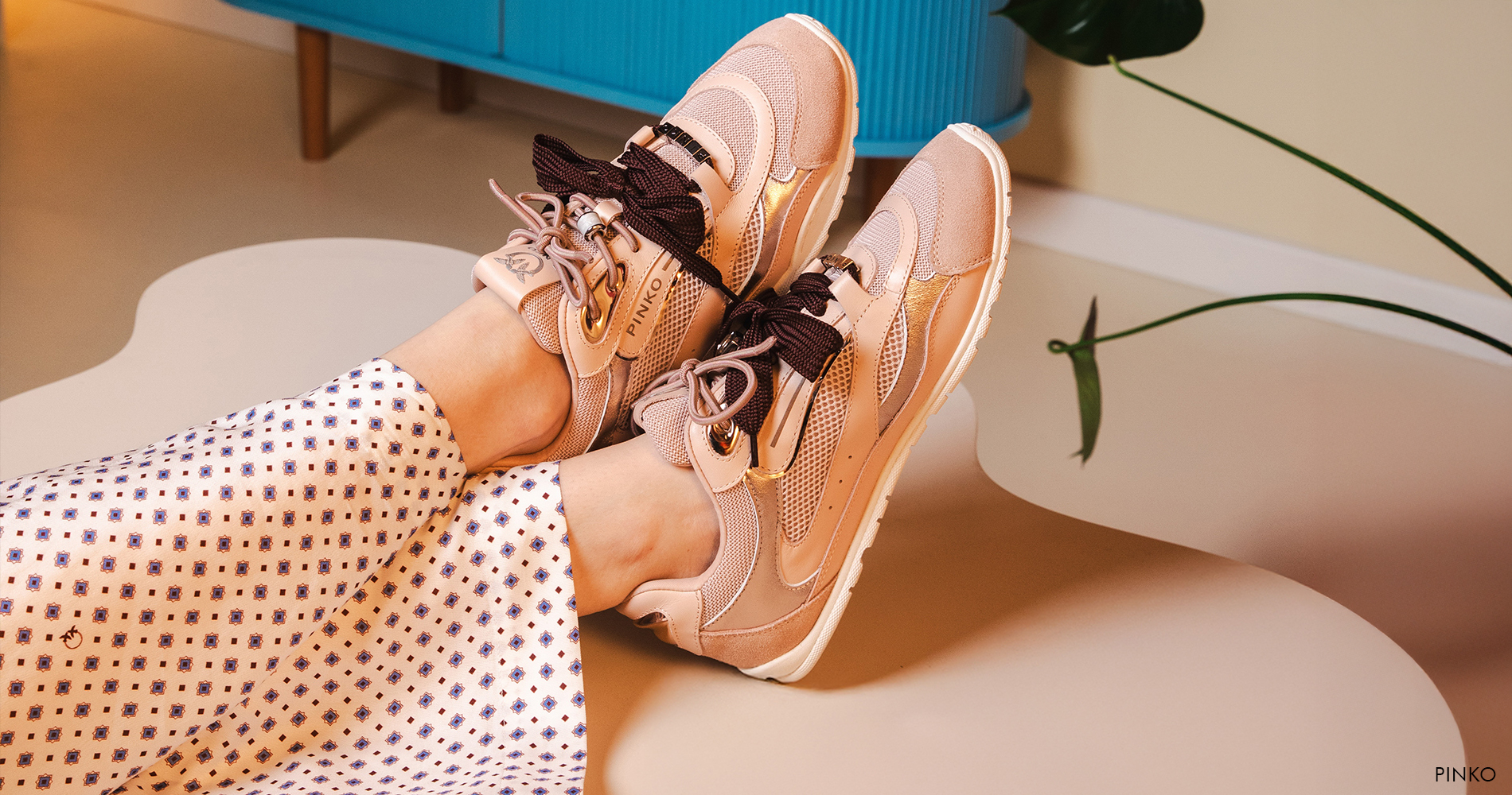 Close-up ženskih stopal, obutih v trendovske nežno roza superge z detajlom satenastih vezalk.
