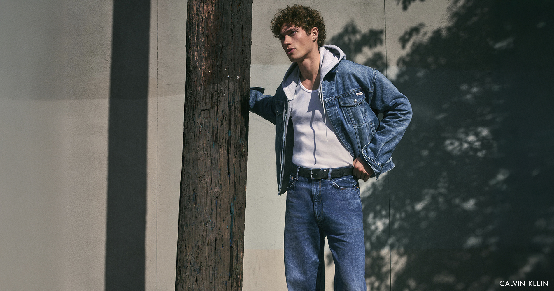 Mlad moški stoji na ulici, oblečen v jeans hlače in denim jakno.