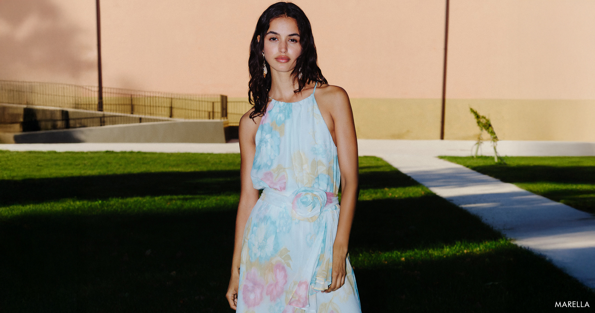 A woman in a light floral dress radiates ease and effortless elegance.