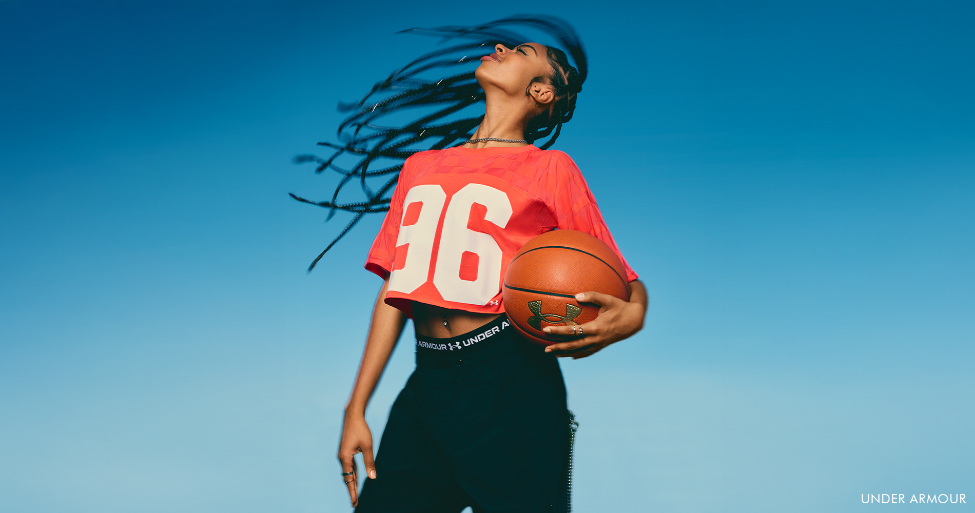 A sporty woman wearing a red crop top with the number 96 and black leggings holds a basketball.