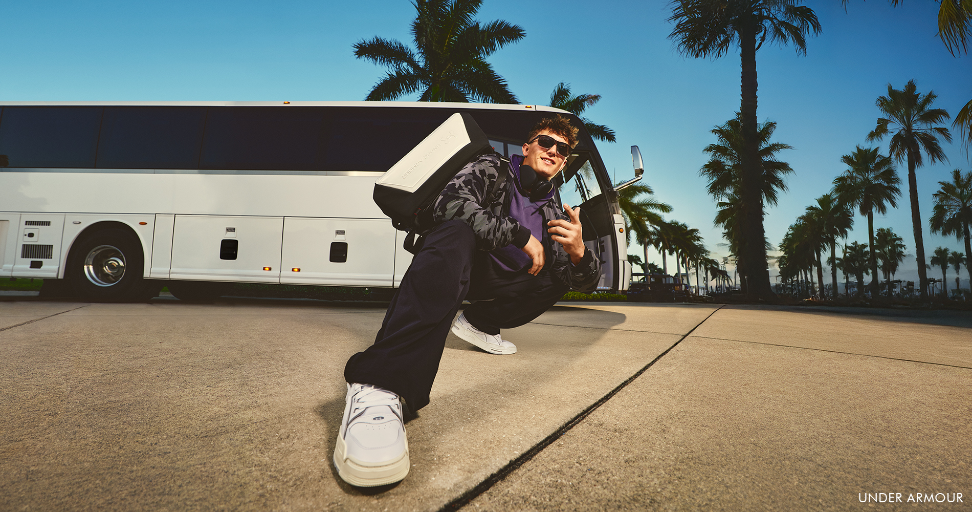 A man in a relaxed streetwear look wears sunglasses and carries a sports bag.
