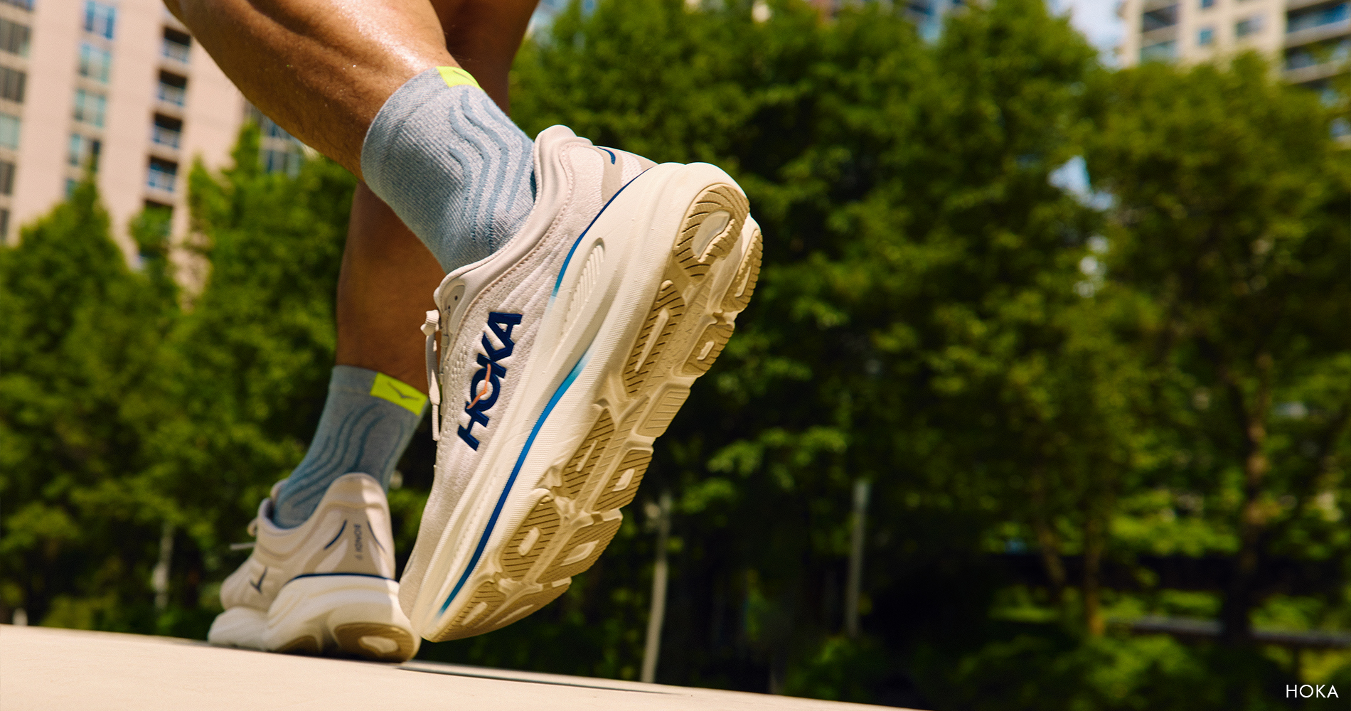 Close-up detail of running shoes in motion, captured during an outdoor run with an urban backdrop and greenery.
