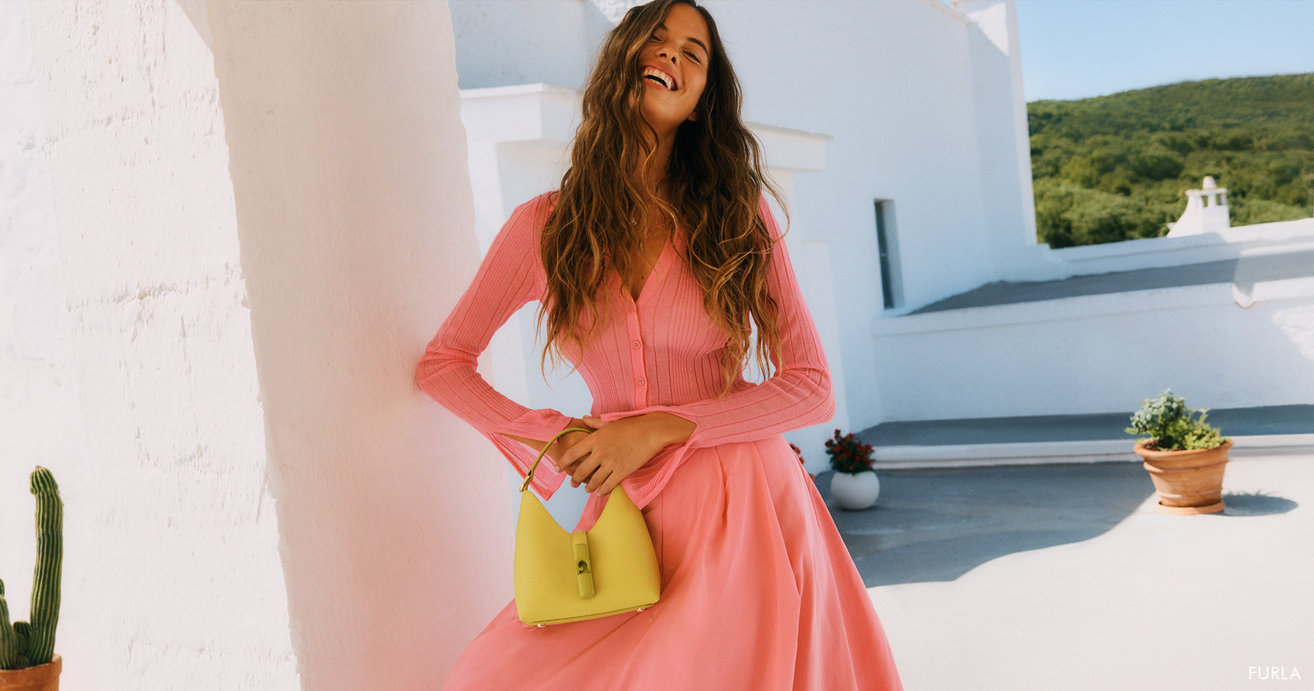 A smiling woman with long hair wearing a vibrant pink cardigan and skirt set.