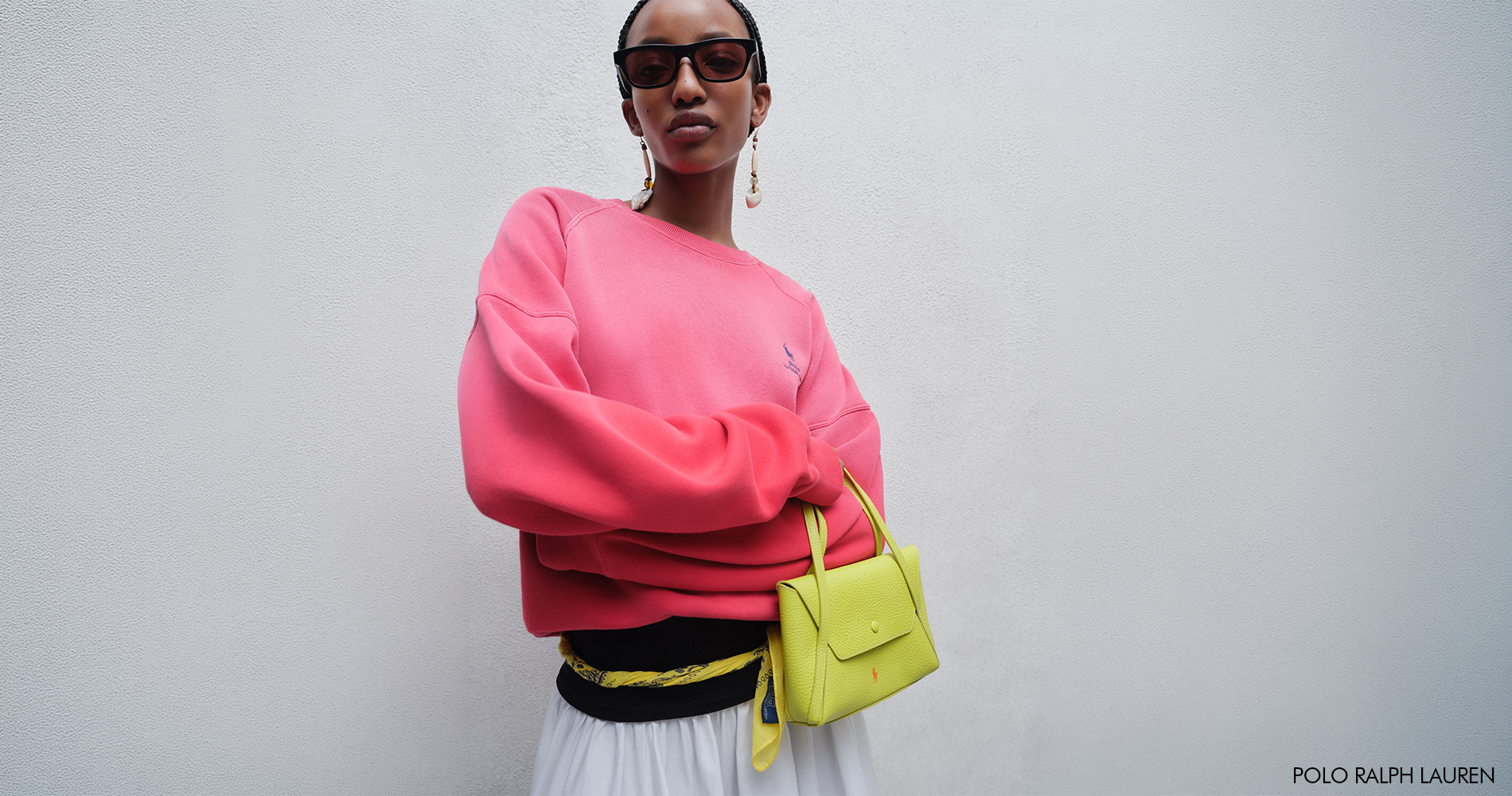 A woman wearing a bright pink sweater with a contrasting neon handbag and sunglasses.